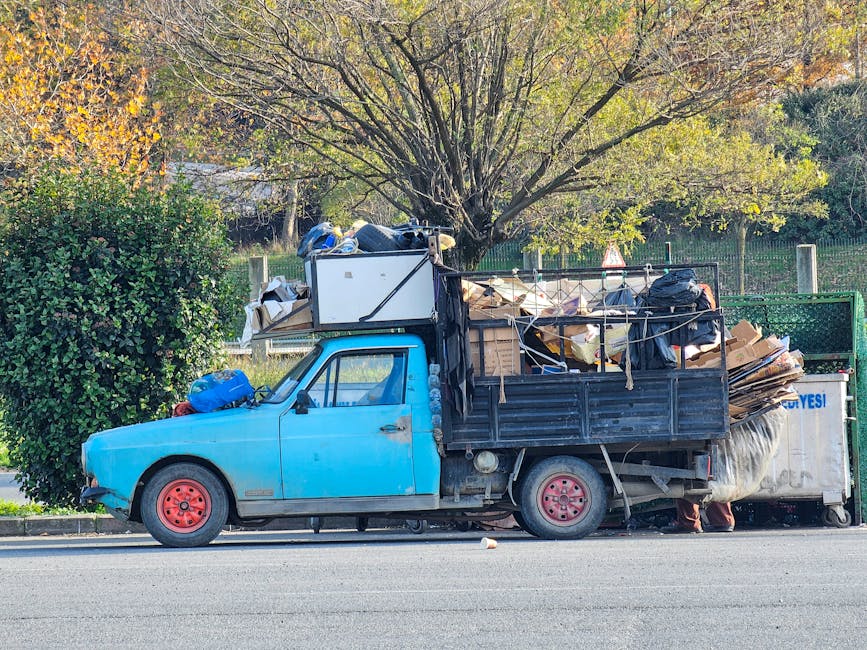 A small burgundy flatbed truck parked on a city street, filled with various types of waste materials including large white and black plastic bags, some of which appear to contain household rubbish or 
